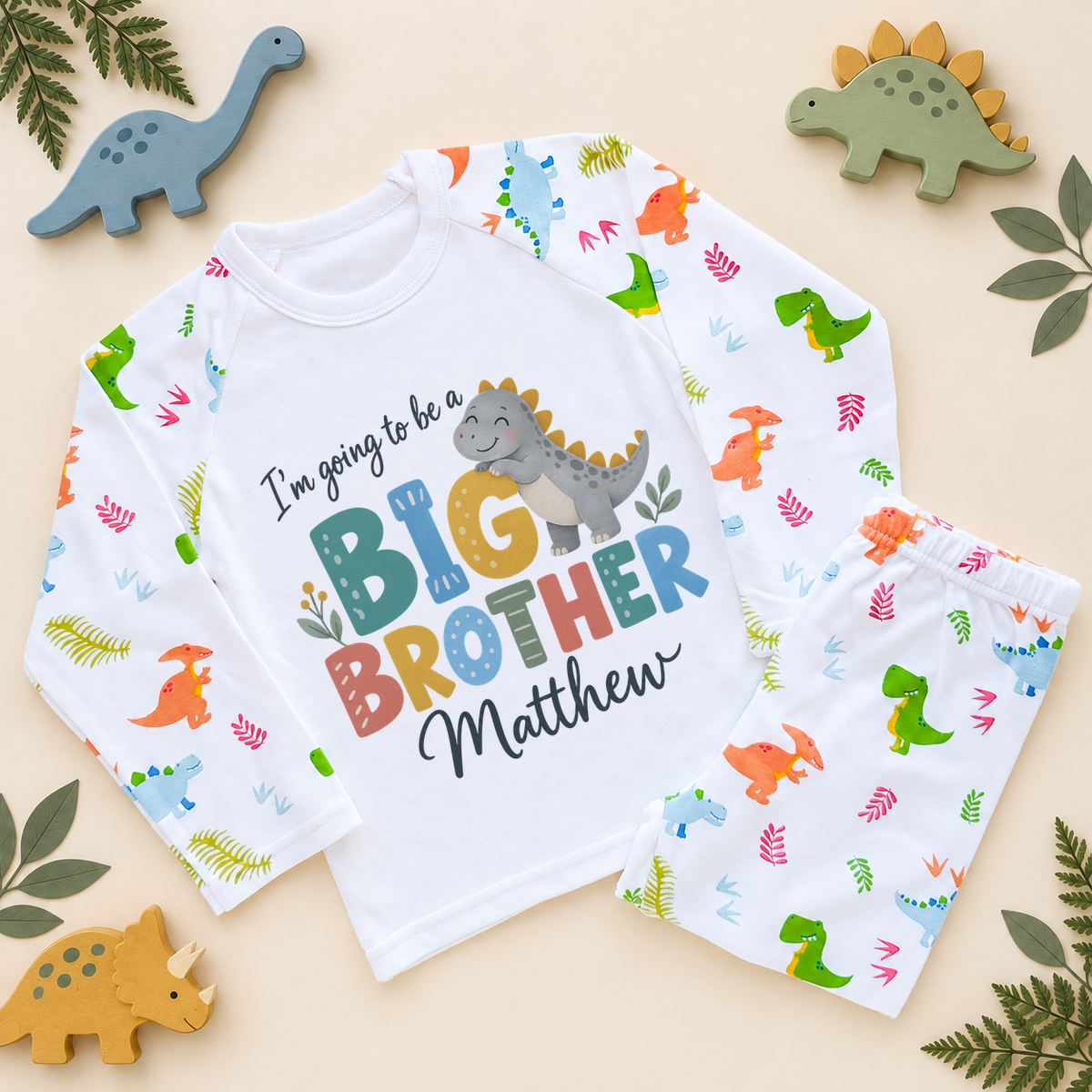 Personalised big brother pyjamas with dino-print sleeves and trousers: a smiling grey dinosaur with mustard spikes hugs the G of I'm going to be a BIG BROTHER, with Matthew as an example name in navy script