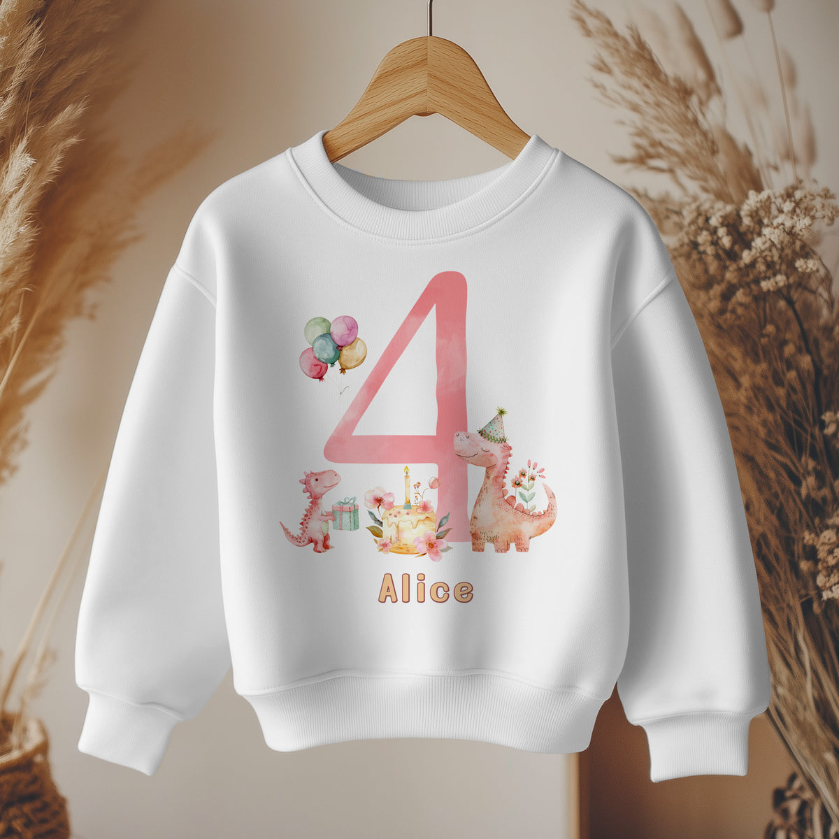 White kids' sweatshirt with a large pink number 4, two pink dinosaurs beside a floral birthday cake, balloons and a name below. Example name shown.