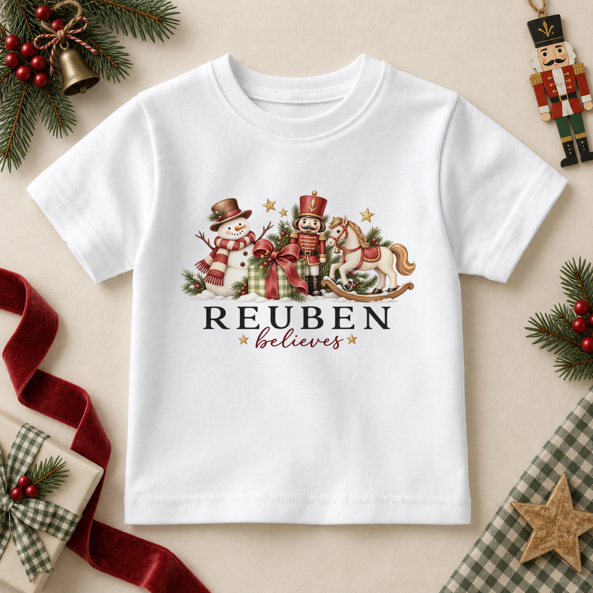 White kids T-shirt with a snowman, nutcracker, rocking horse and ribboned gift. Reuben believes example personalisation.