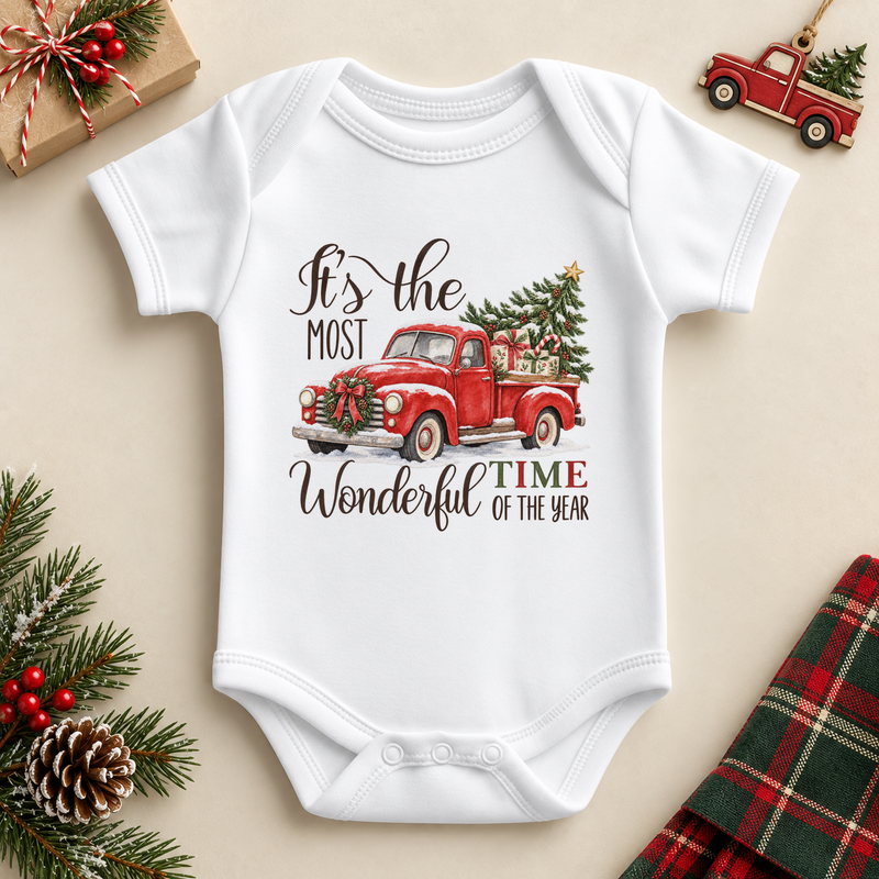 White baby bodysuit with a red vintage pickup carrying a Christmas tree, with festive lettering. It's the most wonderful time of the year wording.