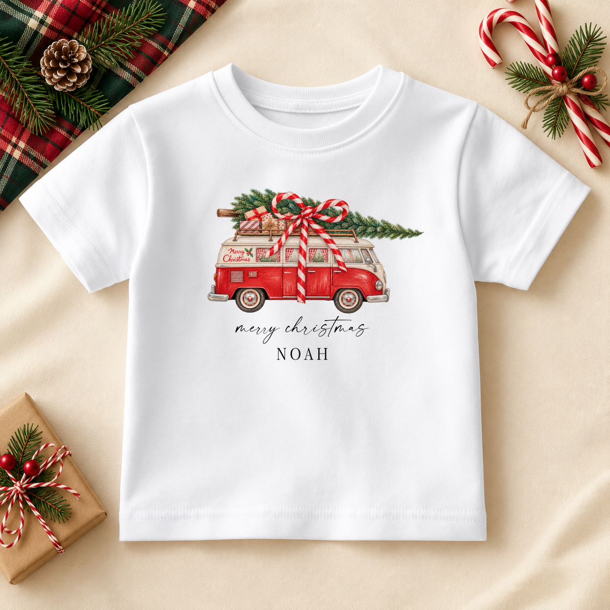 White personalised Christmas T-shirt with a red campervan carrying a tree and presents, Merry Christmas lettering and the name Noah.