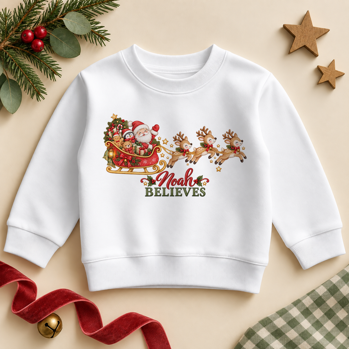 White children's sweatshirt with Santa's sleigh and reindeer, the example name Noah in red script and green Believes lettering.