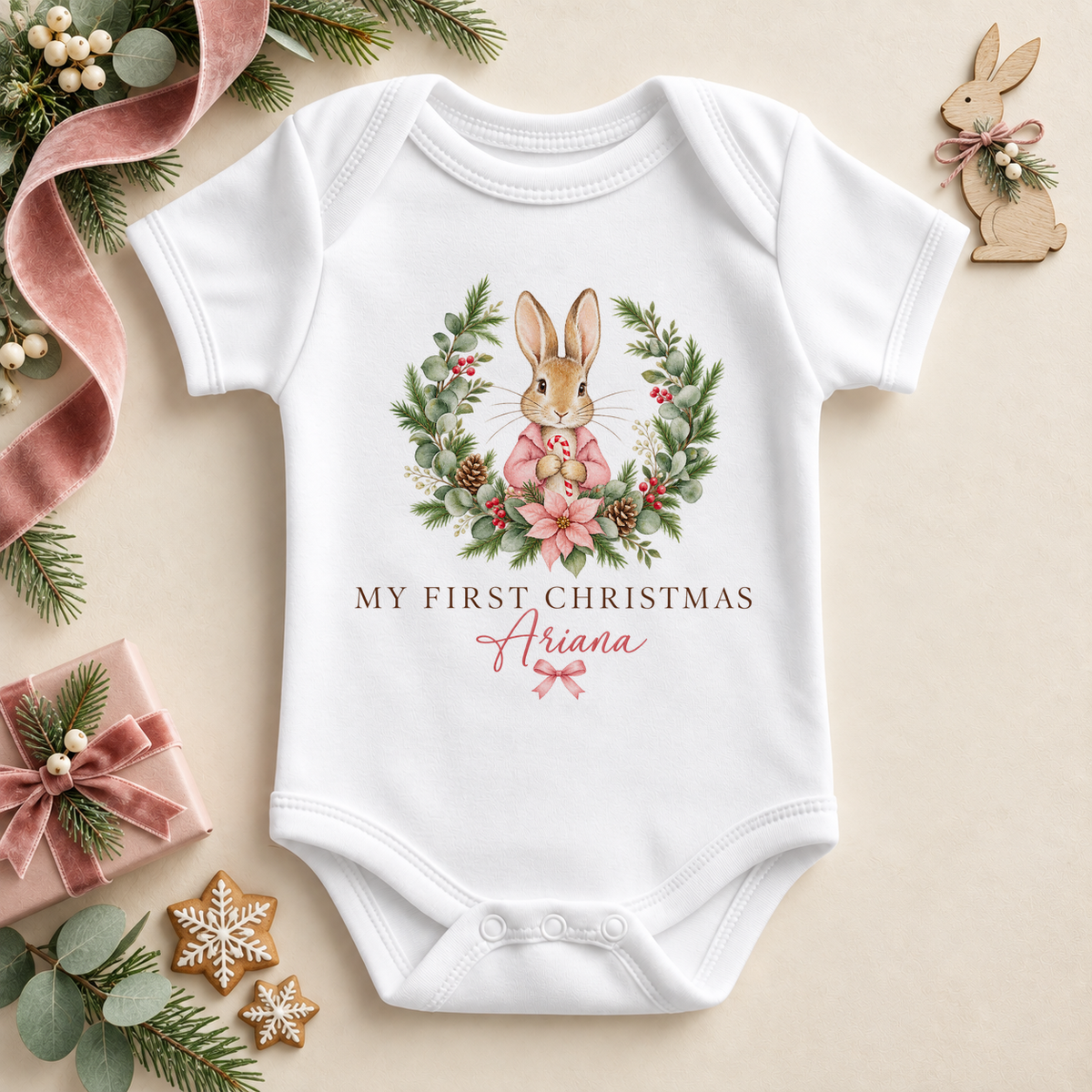 White baby bodysuit. The print features a pink-coated bunny framed by a leafy festive wreath and soft pink flowers.