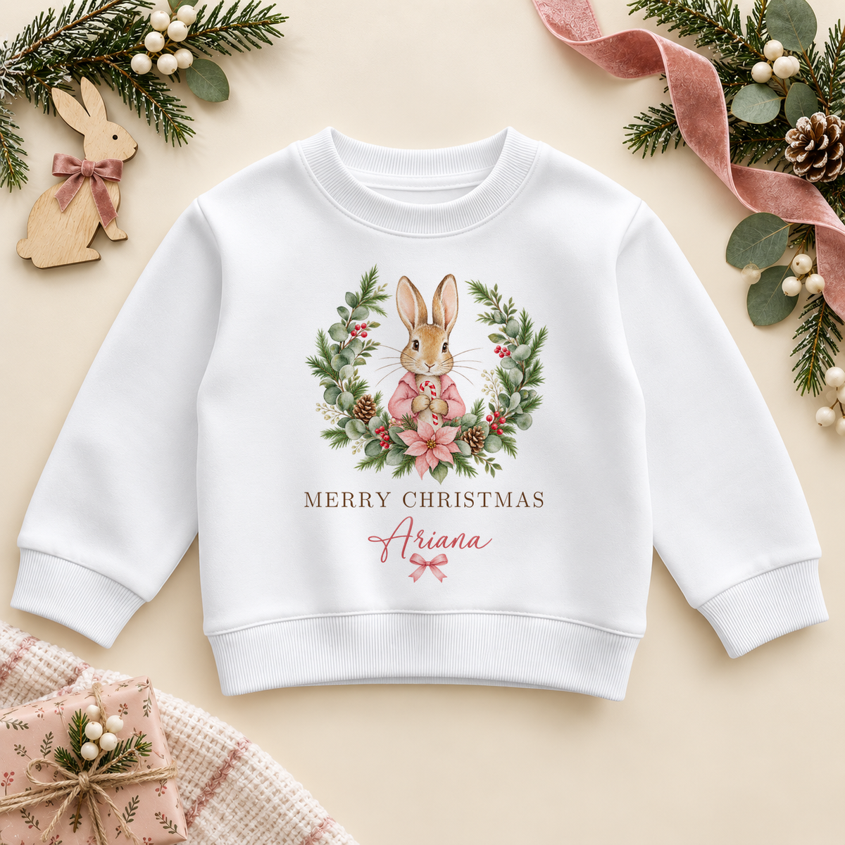 White children’s sweatshirt. The print features a pink-coated bunny framed by a leafy festive wreath and soft pink flowers.