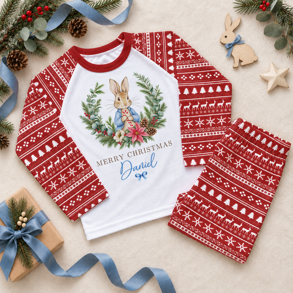 Red and white Christmas pyjama set with a blue-coated bunny framed by a festive wreath with flowers and berries. Merry Christmas wording. Example personalisation shown.
