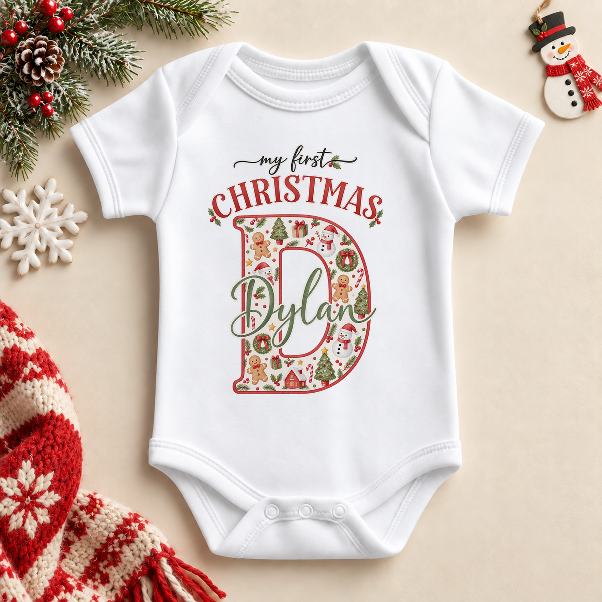 White baby bodysuit. The print features a cream initial filled with little festive motifs and outlined in red.