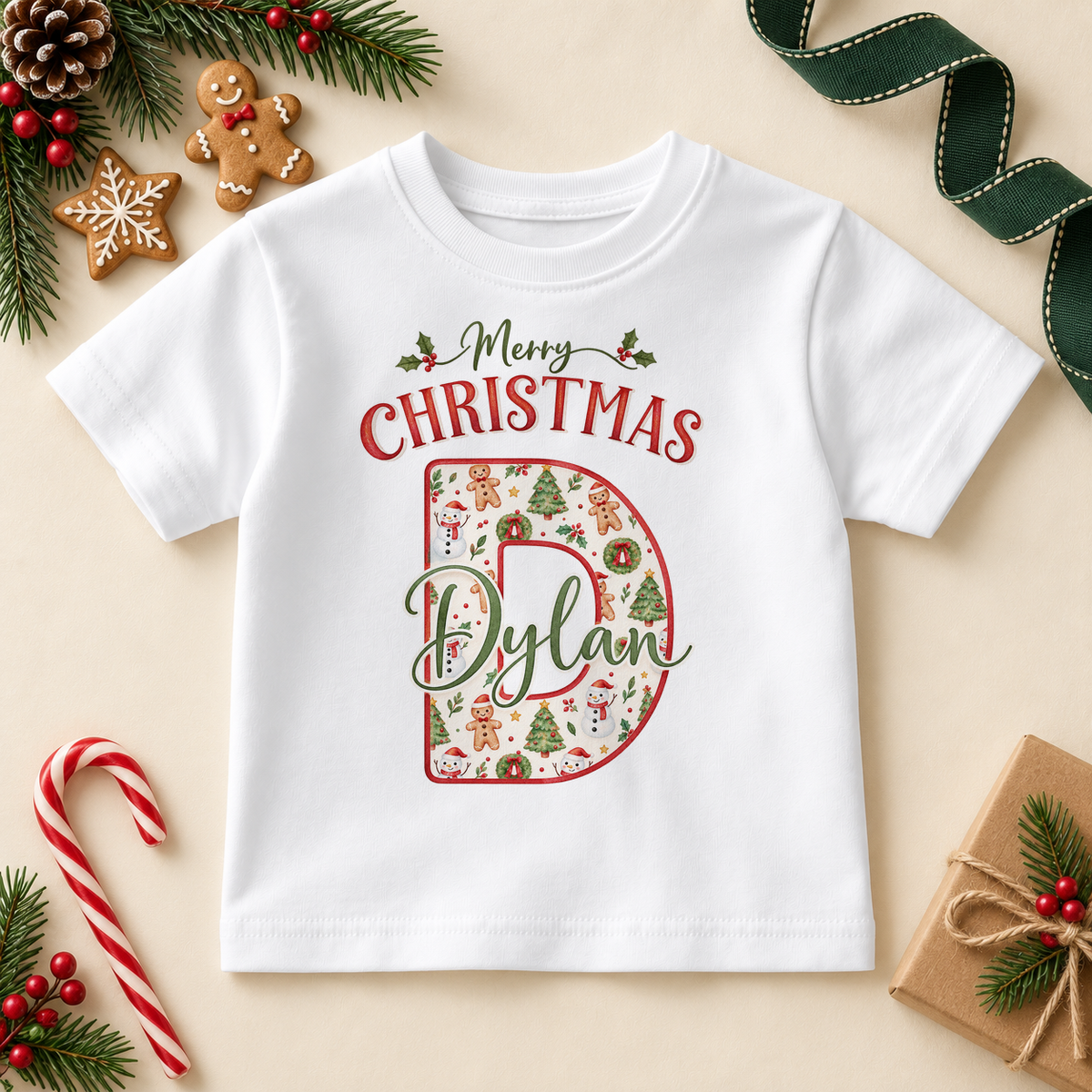 White children’s T-shirt. The print features a cream initial filled with little festive motifs and outlined in red.
