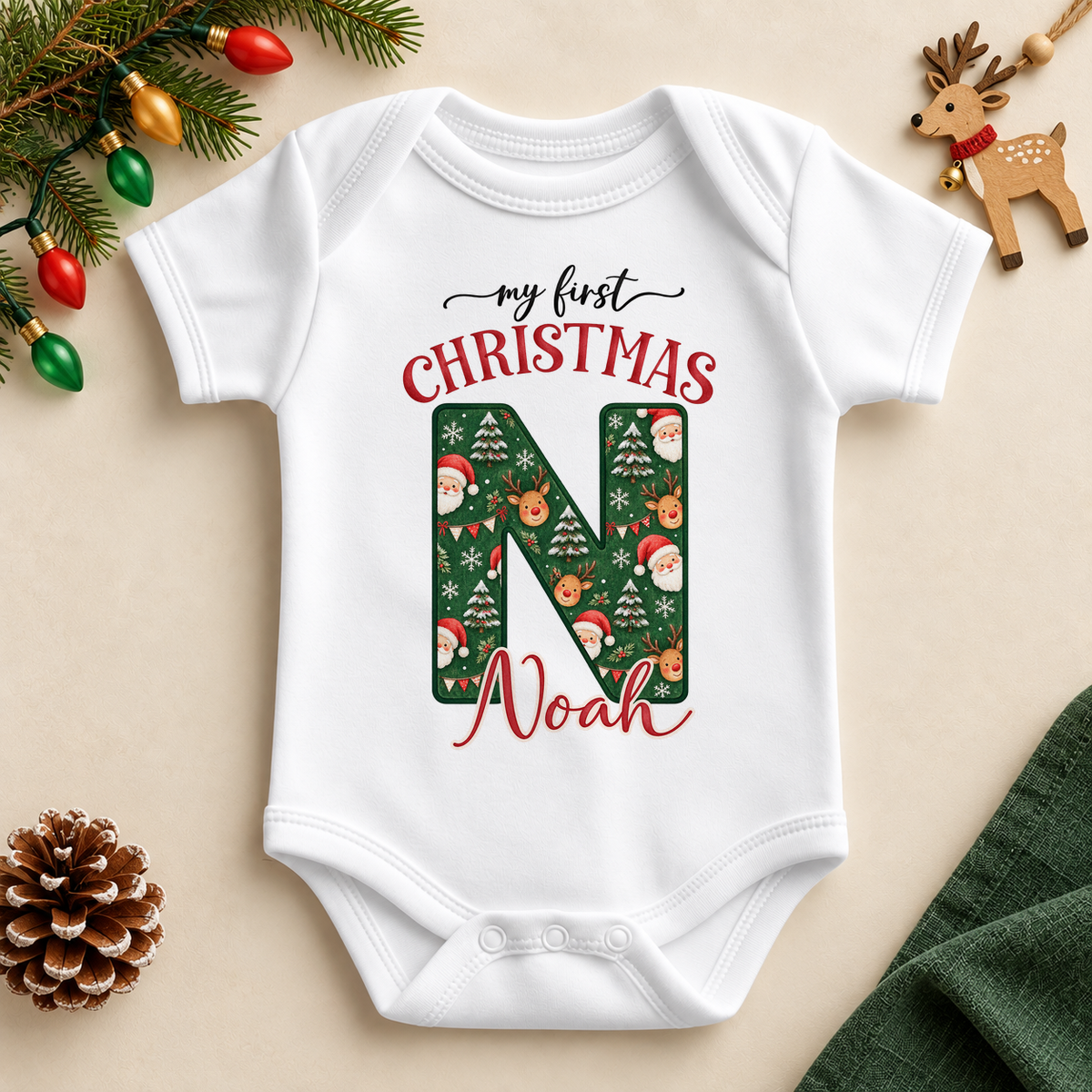 White baby bodysuit. The print features a deep green initial filled with Santa, reindeer and snowy Christmas details.