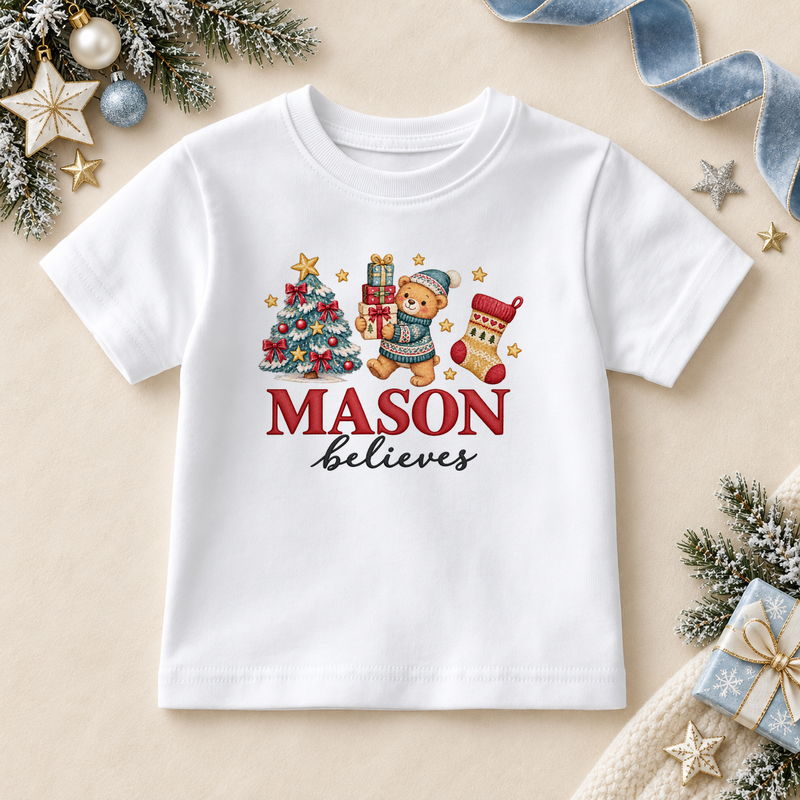 White children’s T-shirt. The print features a teddy in a blue hat holding gifts beside a decorated tree and Christmas stocking.