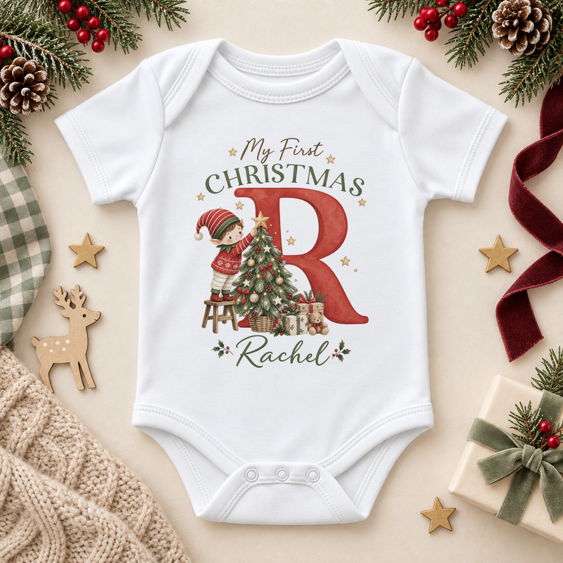 White baby bodysuit. The print features a red initial with a little elf decorating a Christmas tree.