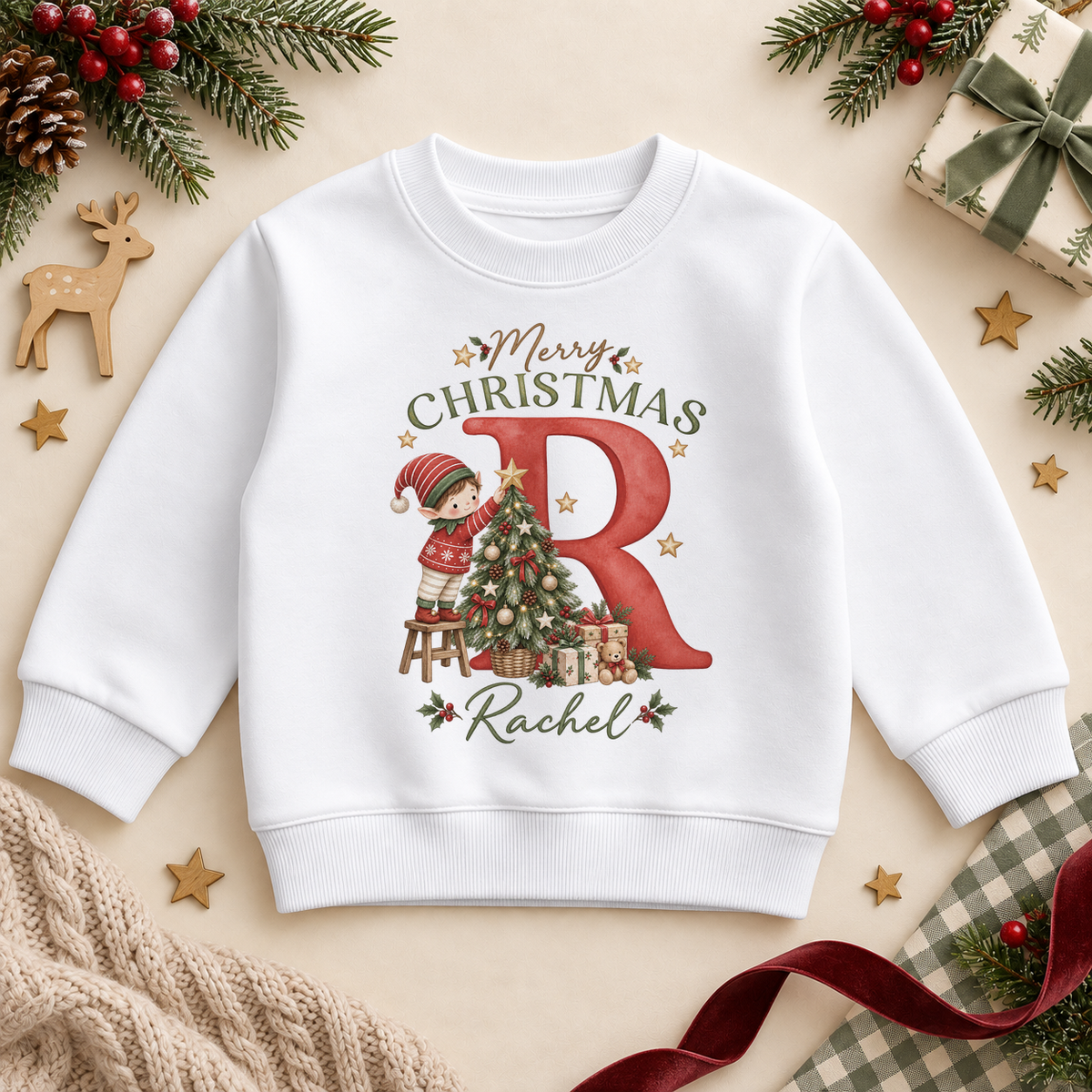 White children’s sweatshirt. The print features a red initial with a little elf decorating a Christmas tree.