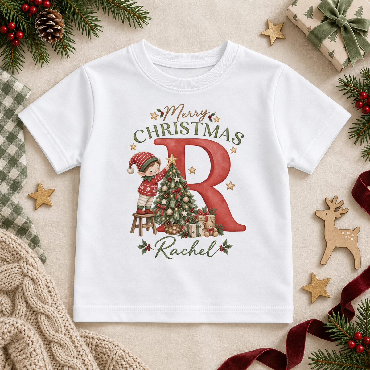 White children’s T-shirt. The print features a red initial with a little elf decorating a Christmas tree.