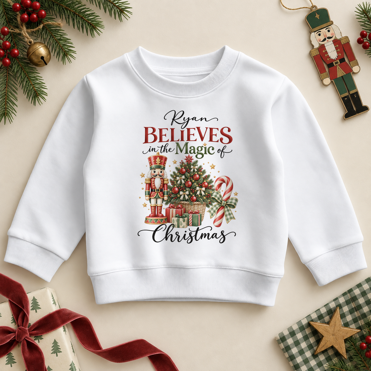 White children’s sweatshirt. The print features a nutcracker, a decorated tree, candy canes and gifts beneath a Christmas belief message.