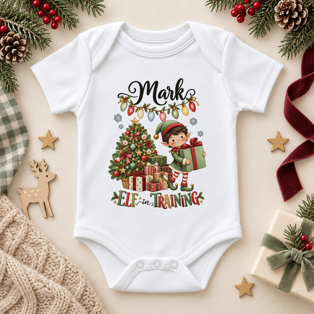 White baby bodysuit. The print features a boy elf carrying a large green present beside a tree and a string of Christmas lights.