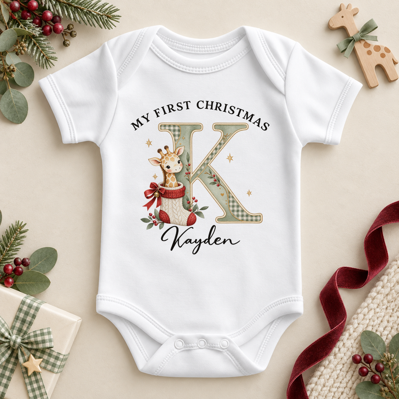 White baby bodysuit. The print features a cream and sage initial beside a giraffe peeking from a knitted Christmas stocking.