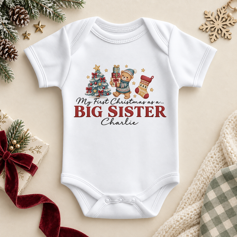White baby bodysuit. The print features a teddy holding gifts beside a tree and stocking above Big Sister lettering.