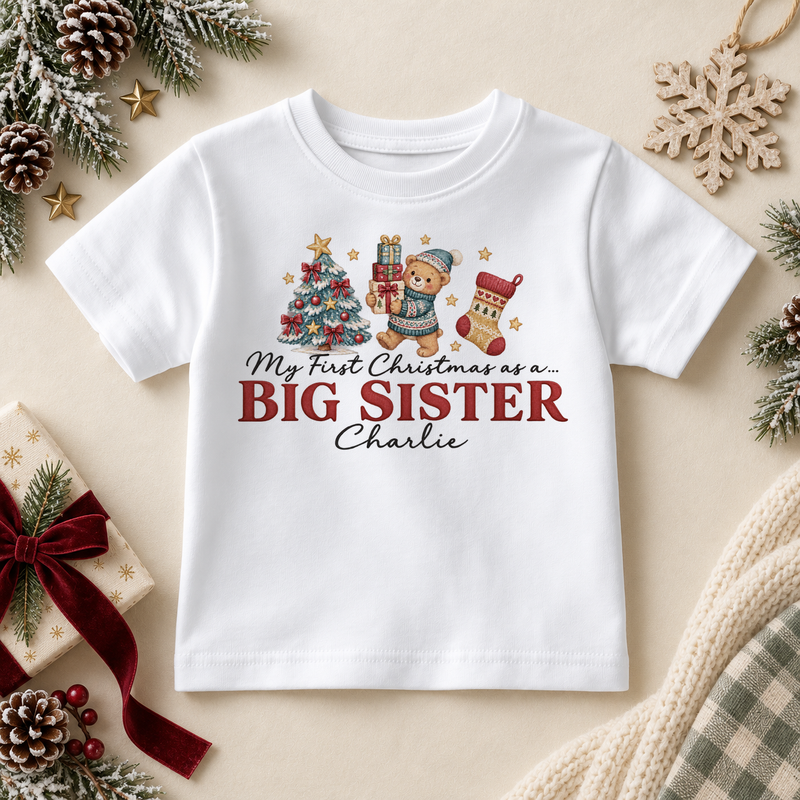 White children’s T-shirt. The print features a teddy holding gifts beside a tree and stocking above Big Sister lettering.