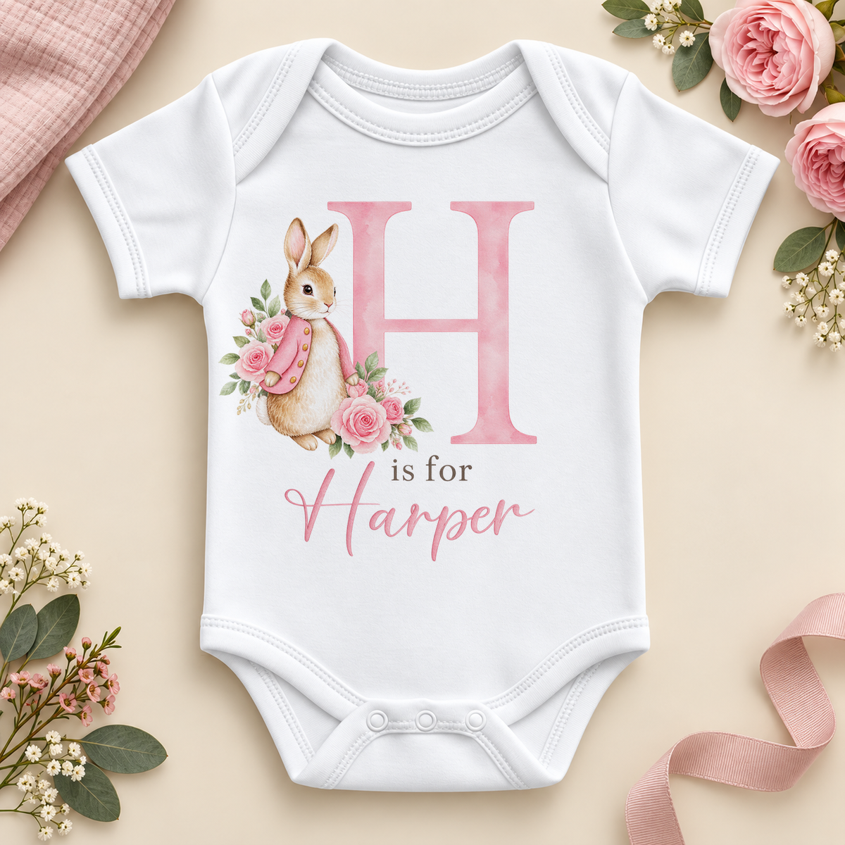 White personalised baby bodysuit with a large pink H initial, a watercolour bunny in a pink jacket with pink roses and H is for Harper as an example name