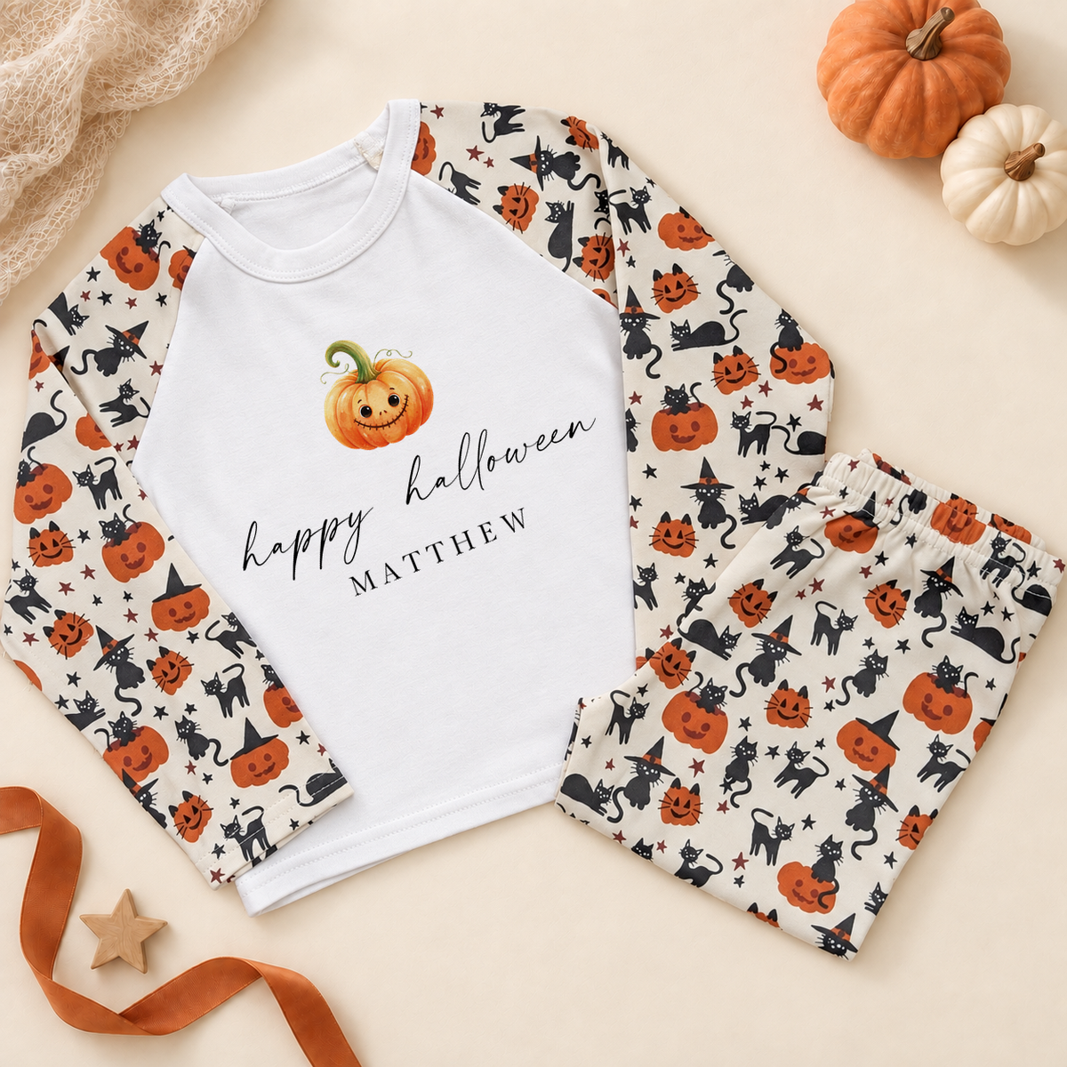 Personalised Halloween pyjama set with smiling pumpkin design, white top and pumpkin-and-cat patterned sleeves and trousers.