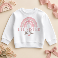 Personalised Lil Sister sweatshirt with a soft pink watercolour rainbow, the name in script and a small heart