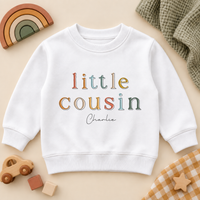 Little Cousin multicolour outlined letters sweatshirt with Charlie example name on a cream flat lay.