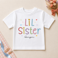 Personalised Lil Sister white T-shirt with colourful outlined letters, hearts and example name Harper.