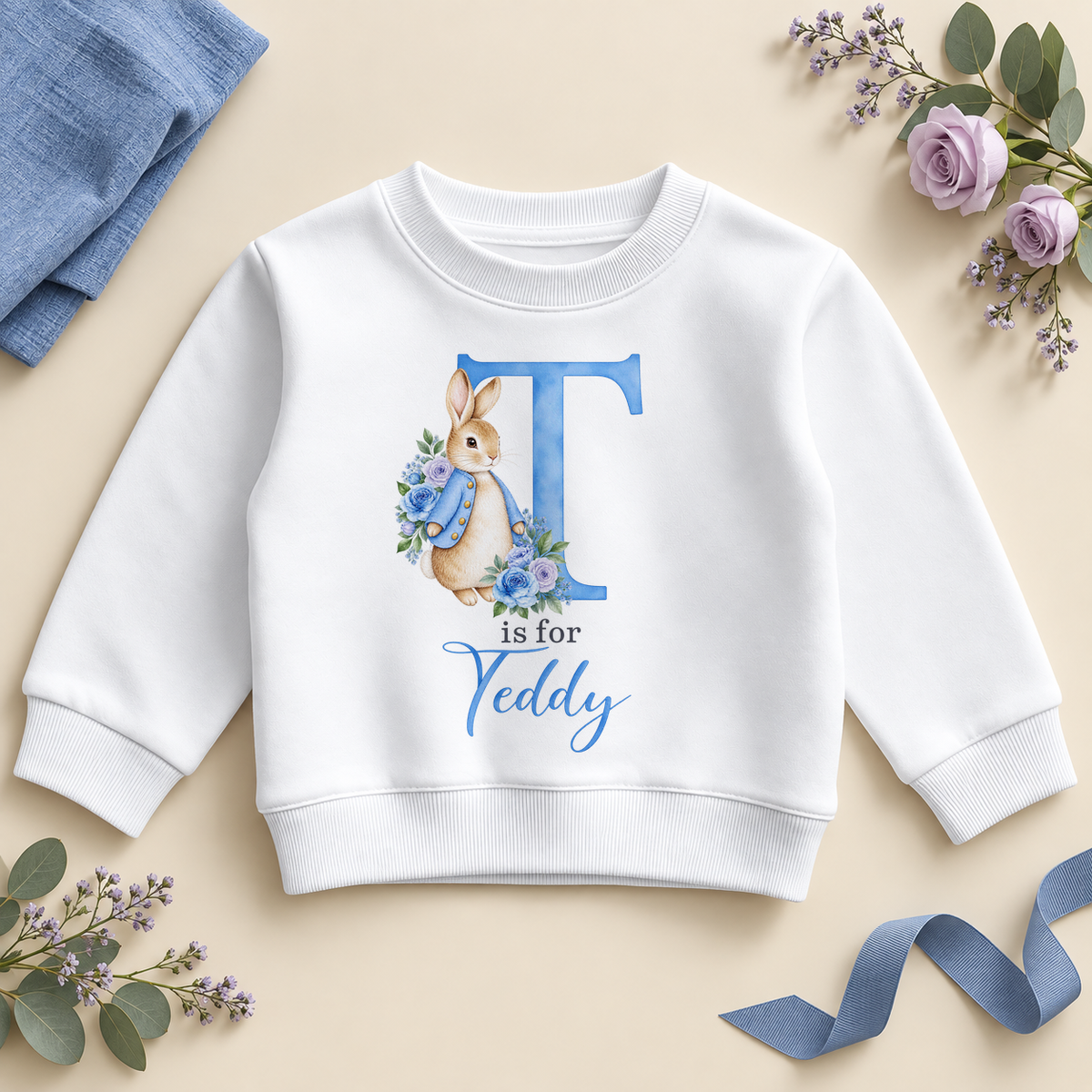 White personalised kids sweatshirt with a large blue T initial, a watercolour bunny in a blue jacket with blue and lilac roses and T is for Teddy as an example name