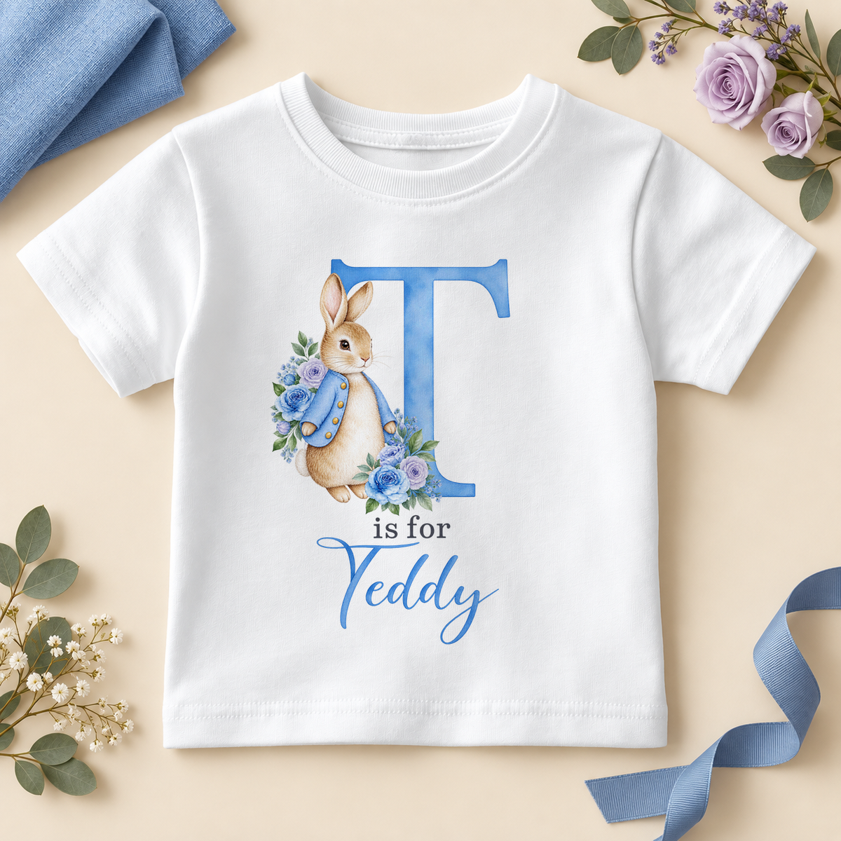 White personalised kids T-shirt with a large blue T initial, a watercolour bunny in a blue jacket with blue and lilac roses and T is for Teddy as an example name