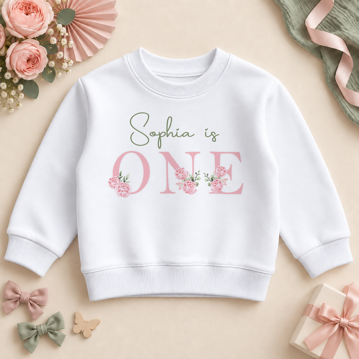 Personalised white first birthday sweatshirt with sage Sophia is script and pink rose ONE lettering, styled with roses, bows and a birthday gift.