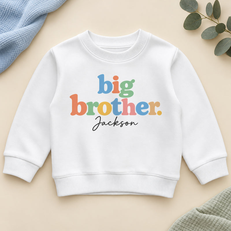 Personalised big brother sweatshirt with big brother in chunky pastel rainbow letters and an example name in black script on a white crew neck sweatshirt