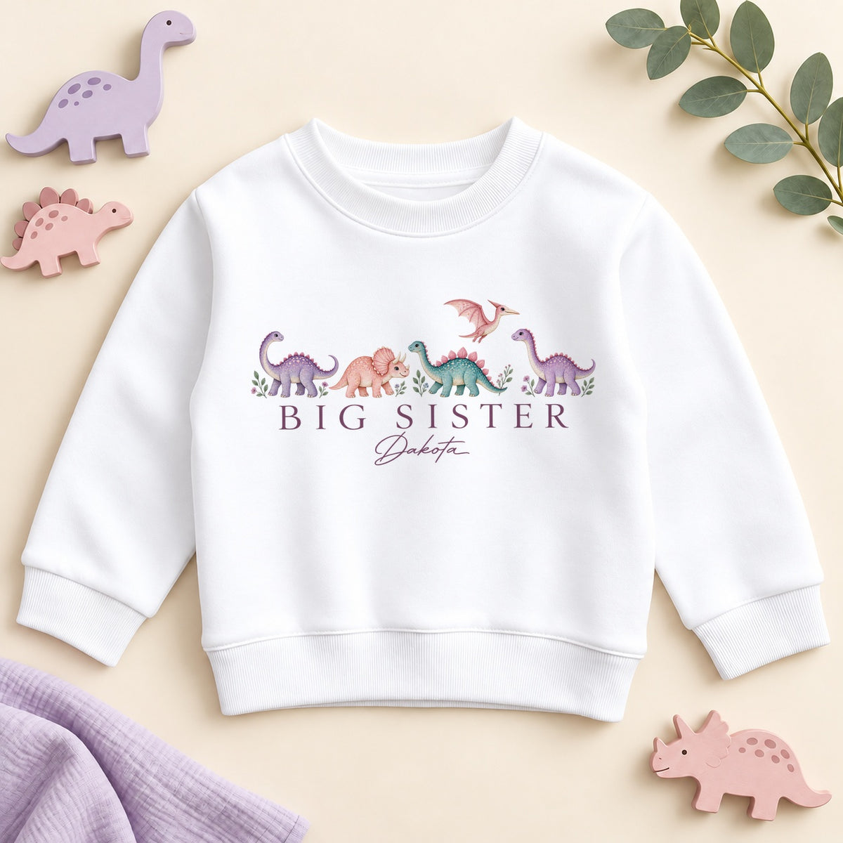 Personalised big sister sweatshirt with pastel dinosaurs, big sister in plum capitals and an example name in script on a white crew neck dino jumper
