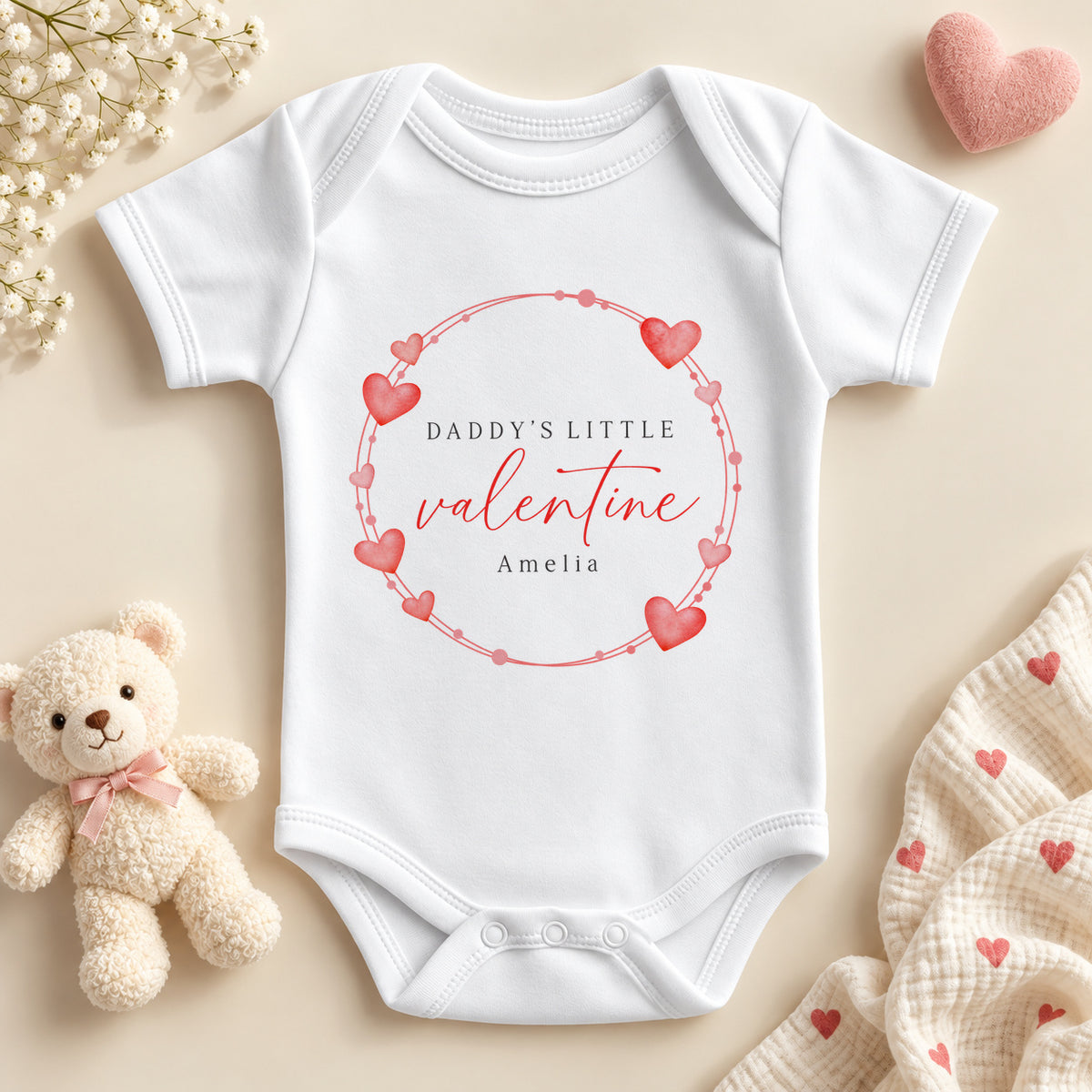 Personalised Daddy's little valentine baby bodysuit: a white baby vest with a wreath of red and pink hearts, red script and an example name