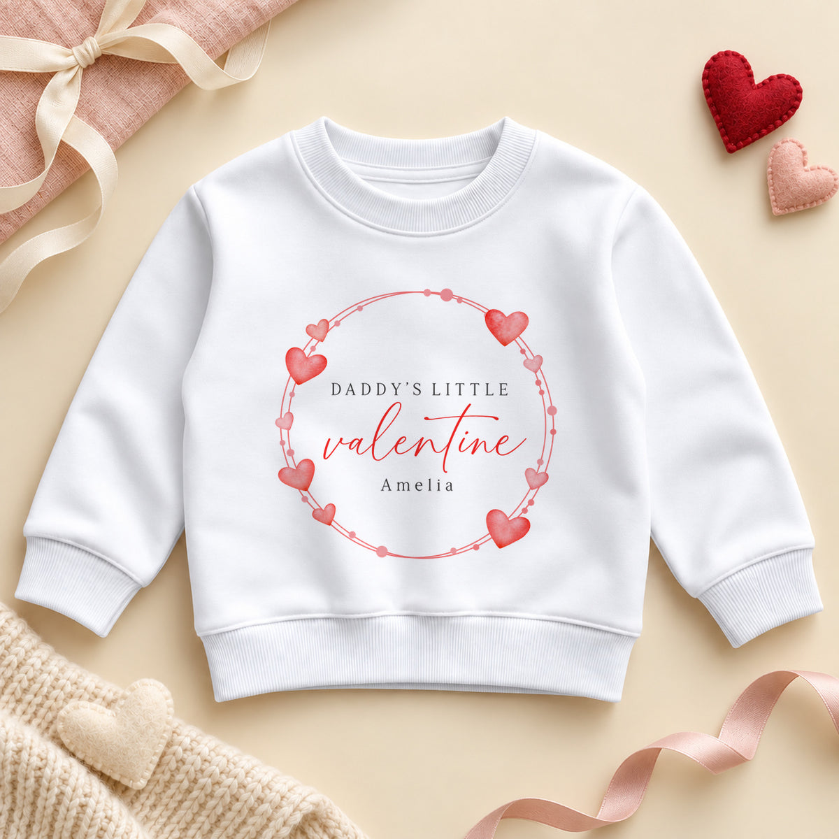 Personalised Daddy's little valentine toddler sweatshirt: a white jumper with a wreath of red and pink hearts, red script and an example name