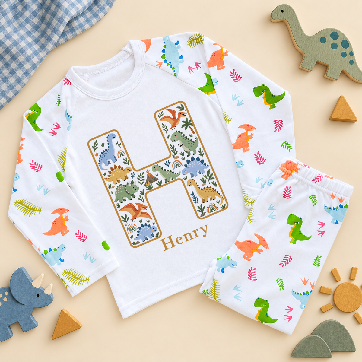 White kids pyjama set with a mustard outlined dinosaur initial H and example name Henry on the top, and colourful dino print raglan sleeves and trousers.