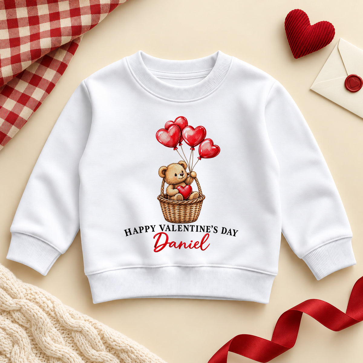 Personalised Happy Valentine's Day toddler sweatshirt: a white jumper with a teddy bear in a wicker basket holding red heart balloons and an example name