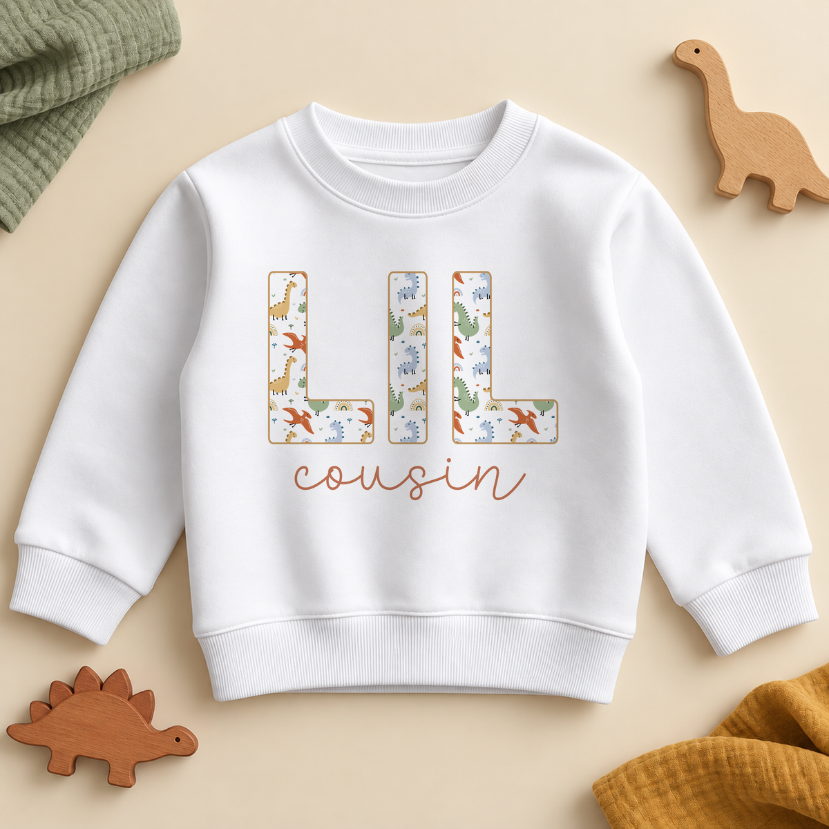 Lil cousin dino sweatshirt with LIL in capital letters filled with a cartoon dinosaur and rainbow print and cousin in terracotta script on a white crew neck sweatshirt