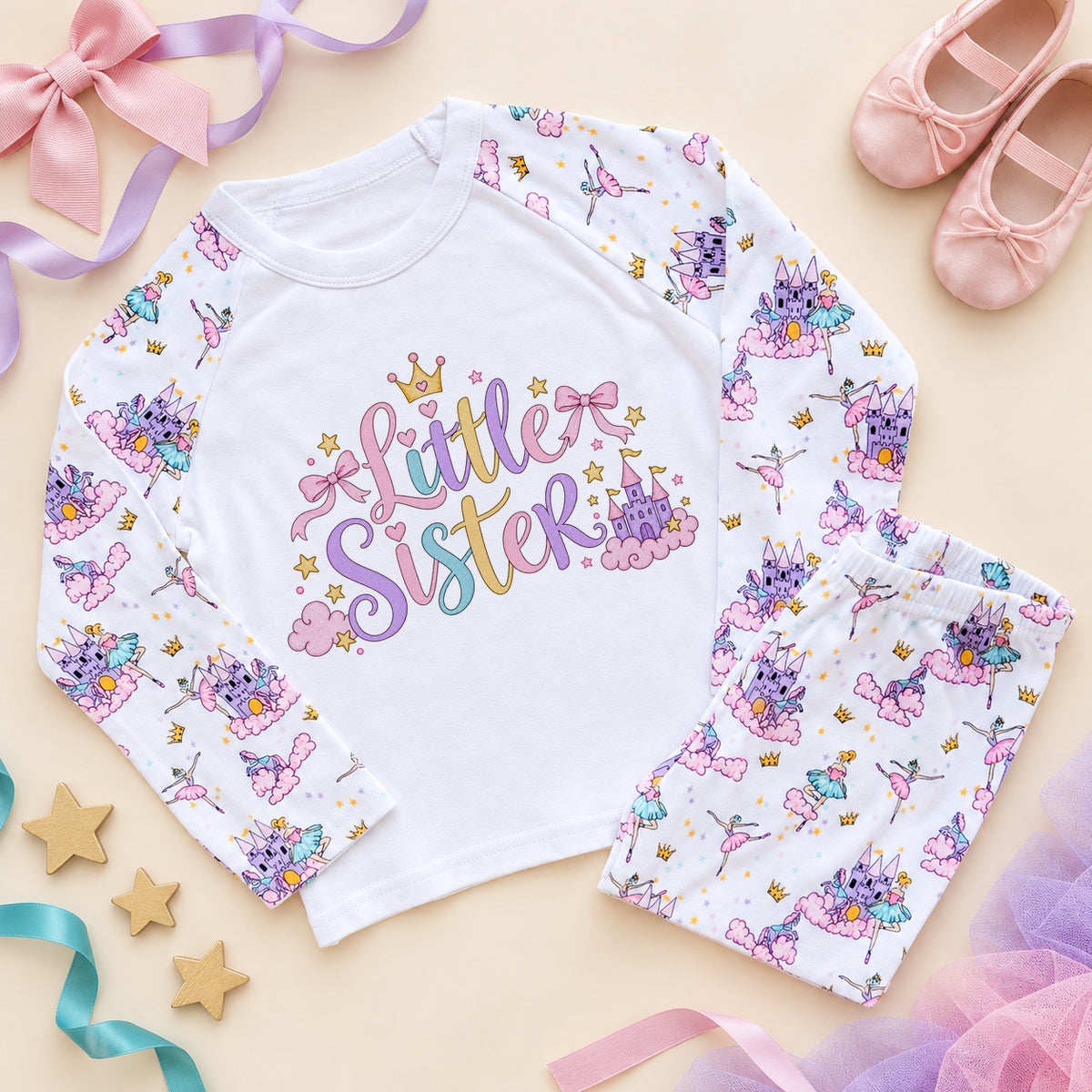 Little sister pyjamas with pastel script lettering, a gold crown, pink bows and a fairy castle on a white chest, with ballerina and princess castle print raglan sleeves and trousers