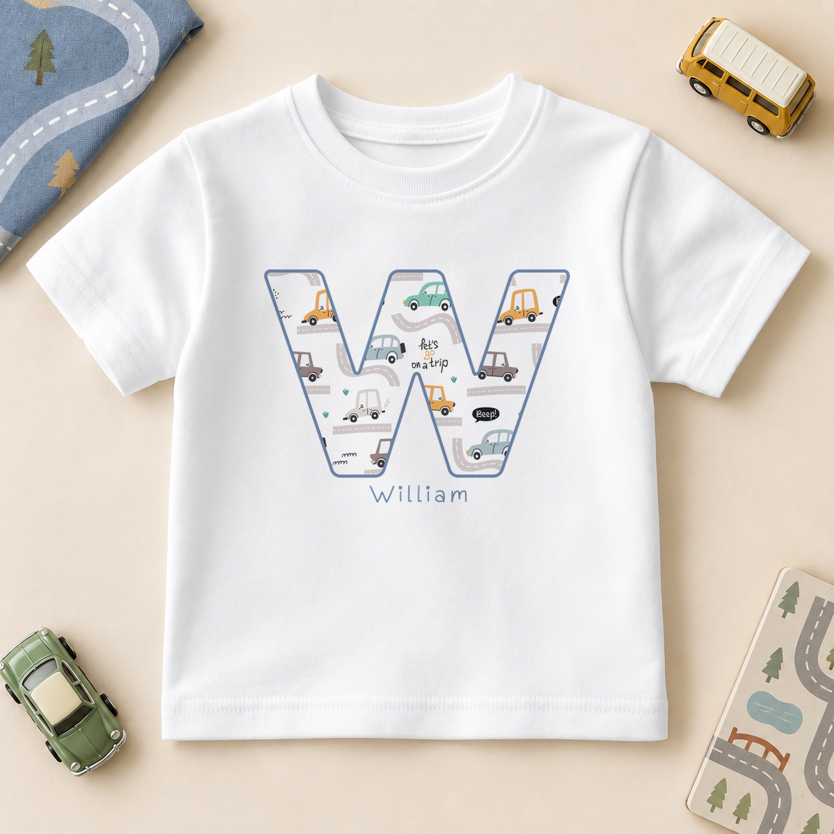 White kids T-shirt with blue-outlined initial W filled with small cars and roads, personalised with the example name William.