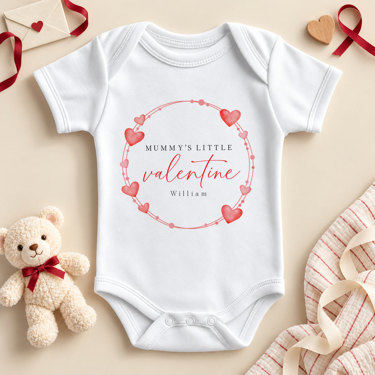 Personalised Mummy's little valentine baby bodysuit: a white baby vest with a wreath of red and pink hearts, red script and an example name