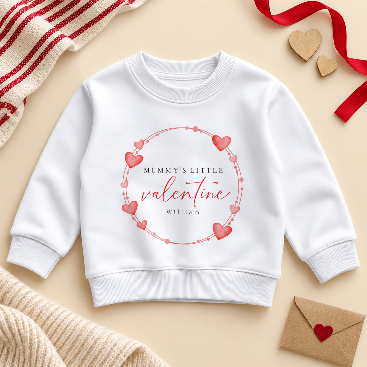 Personalised Mummy's little valentine toddler sweatshirt: a white jumper with a wreath of red and pink hearts, red script and an example name