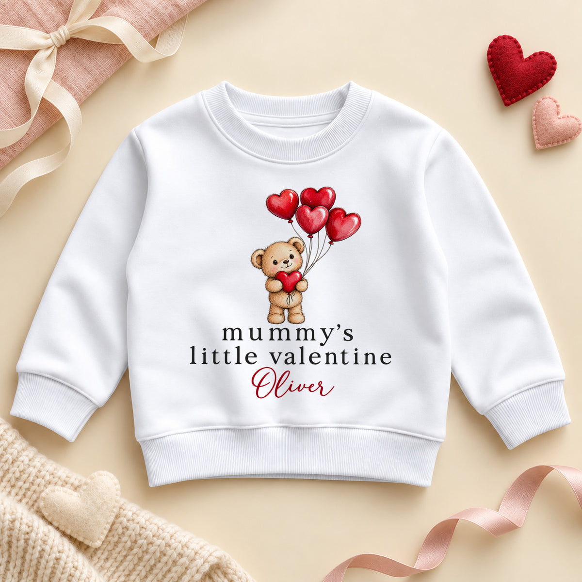Personalised Mummy's little valentine toddler sweatshirt: a white jumper with a teddy bear holding red heart balloons and an example name in red script