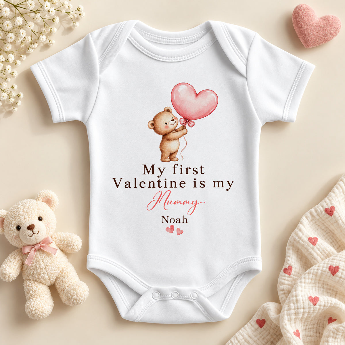 Personalised my first Valentine is my Mummy baby bodysuit: a white baby vest with a teddy bear holding a pink heart balloon, pink script and an example name