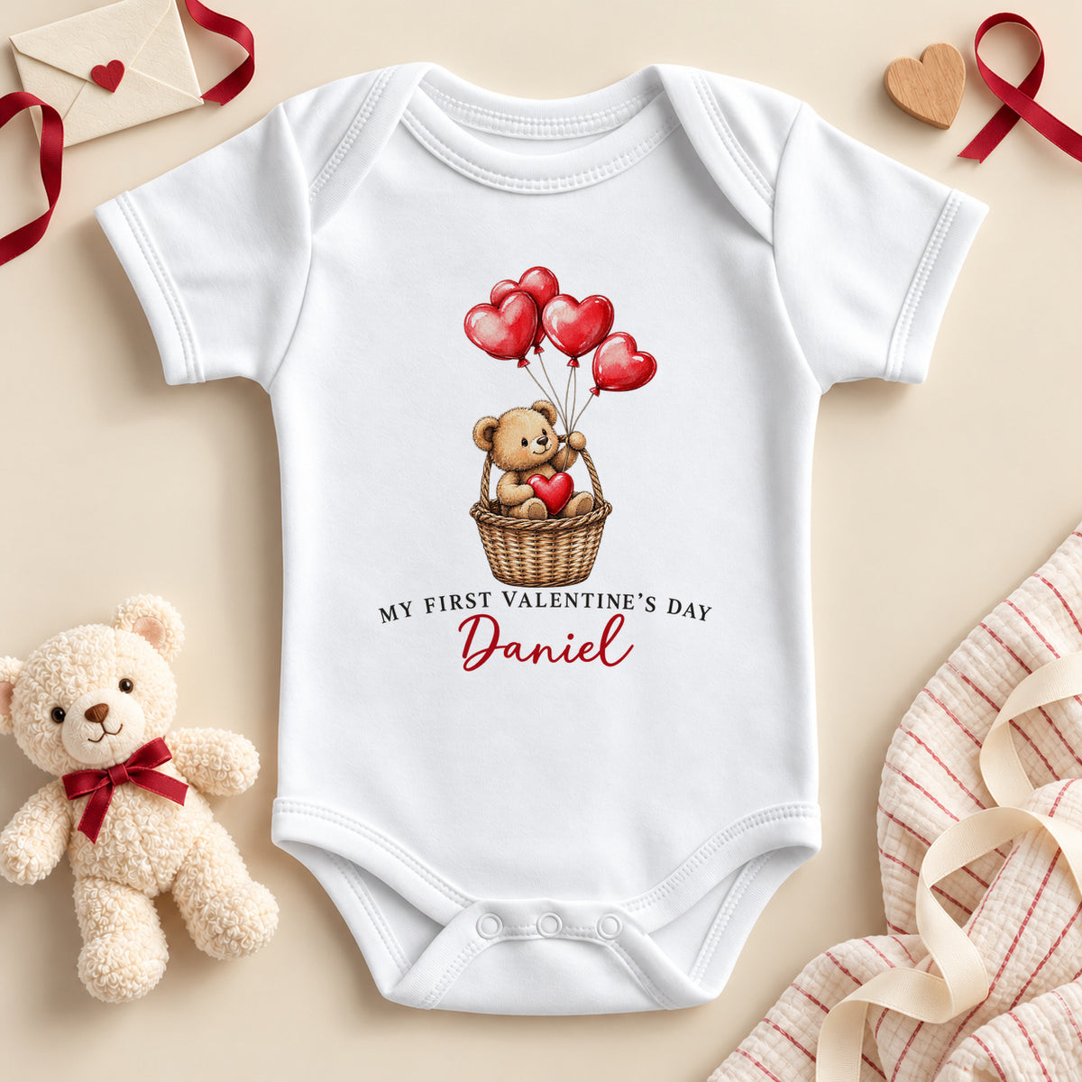 Personalised My First Valentine's Day baby bodysuit: a white baby vest with a teddy bear in a wicker basket holding red heart balloons and an example name