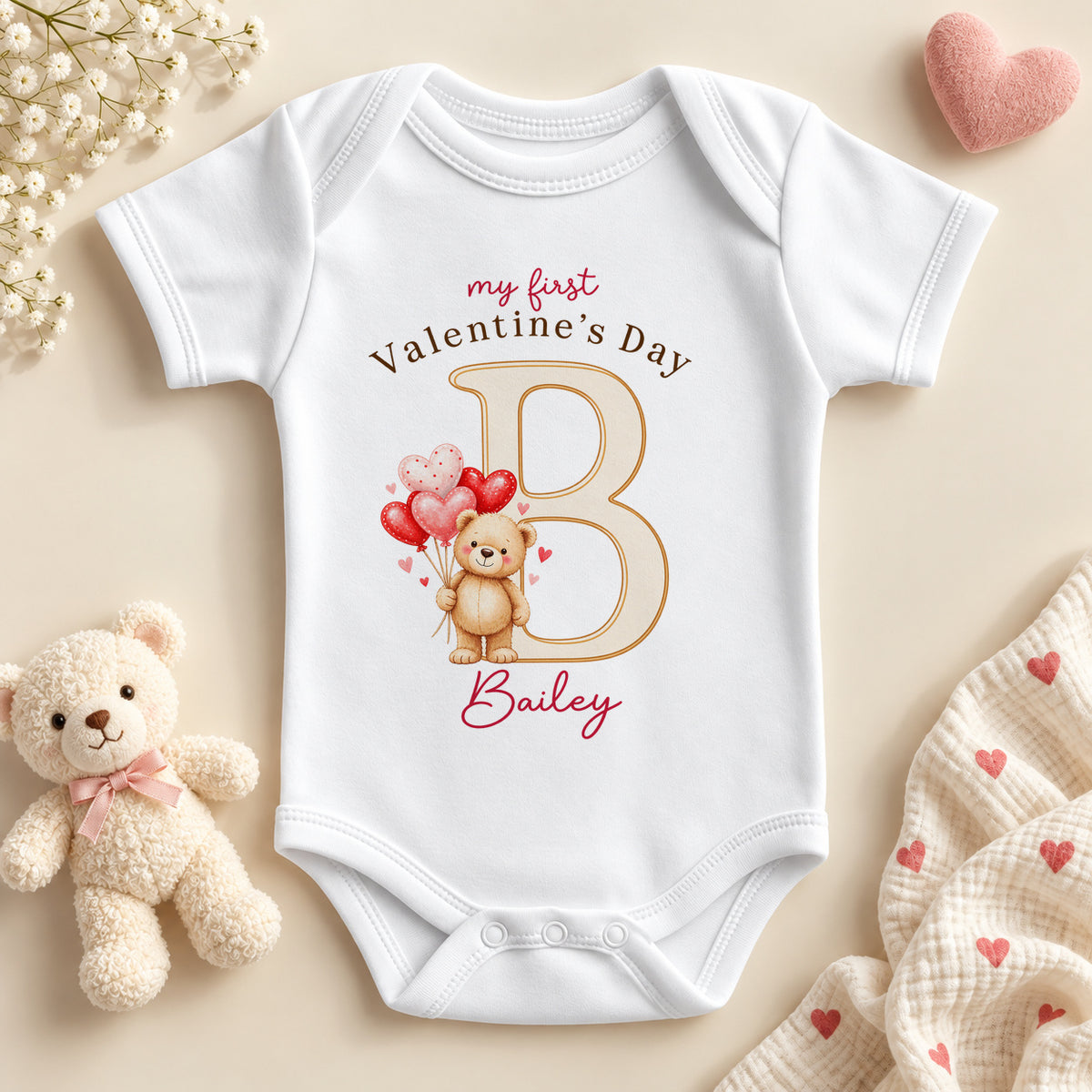Personalised my first Valentine's Day baby bodysuit: a white baby vest with a teddy bear holding heart balloons, a large initial letter and an example name