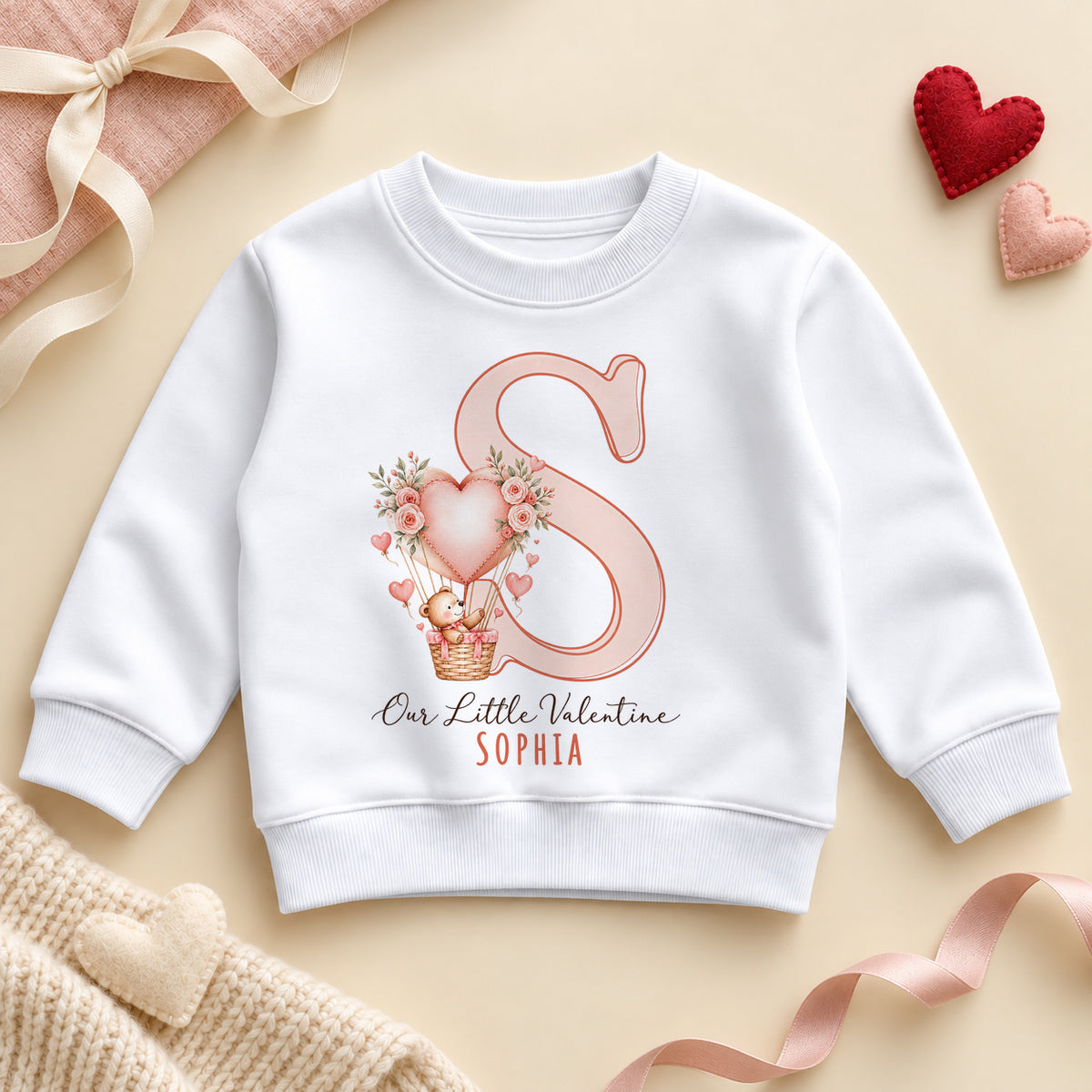 Personalised Our Little Valentine toddler sweatshirt: a white jumper with a large pink initial, a teddy bear in a heart balloon with roses and an example name