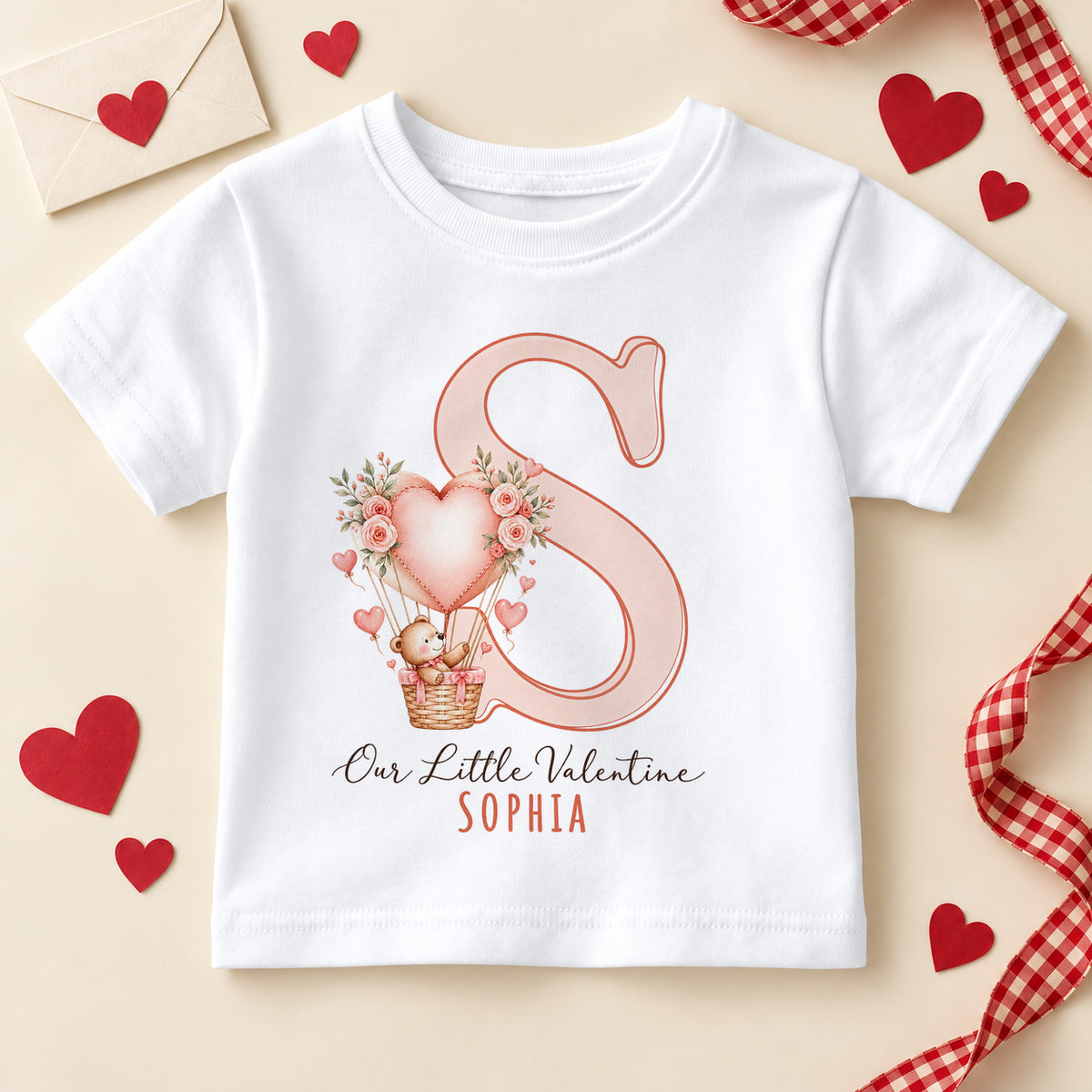Personalised Our Little Valentine kids T-shirt: a white tee with a large pink initial, a teddy bear in a heart balloon with roses and an example name