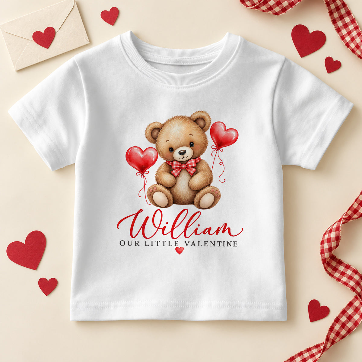 Personalised Our Little Valentine kids T-shirt: a white tee with a teddy bear in a red bow tie between two red heart balloons and an example name in red script