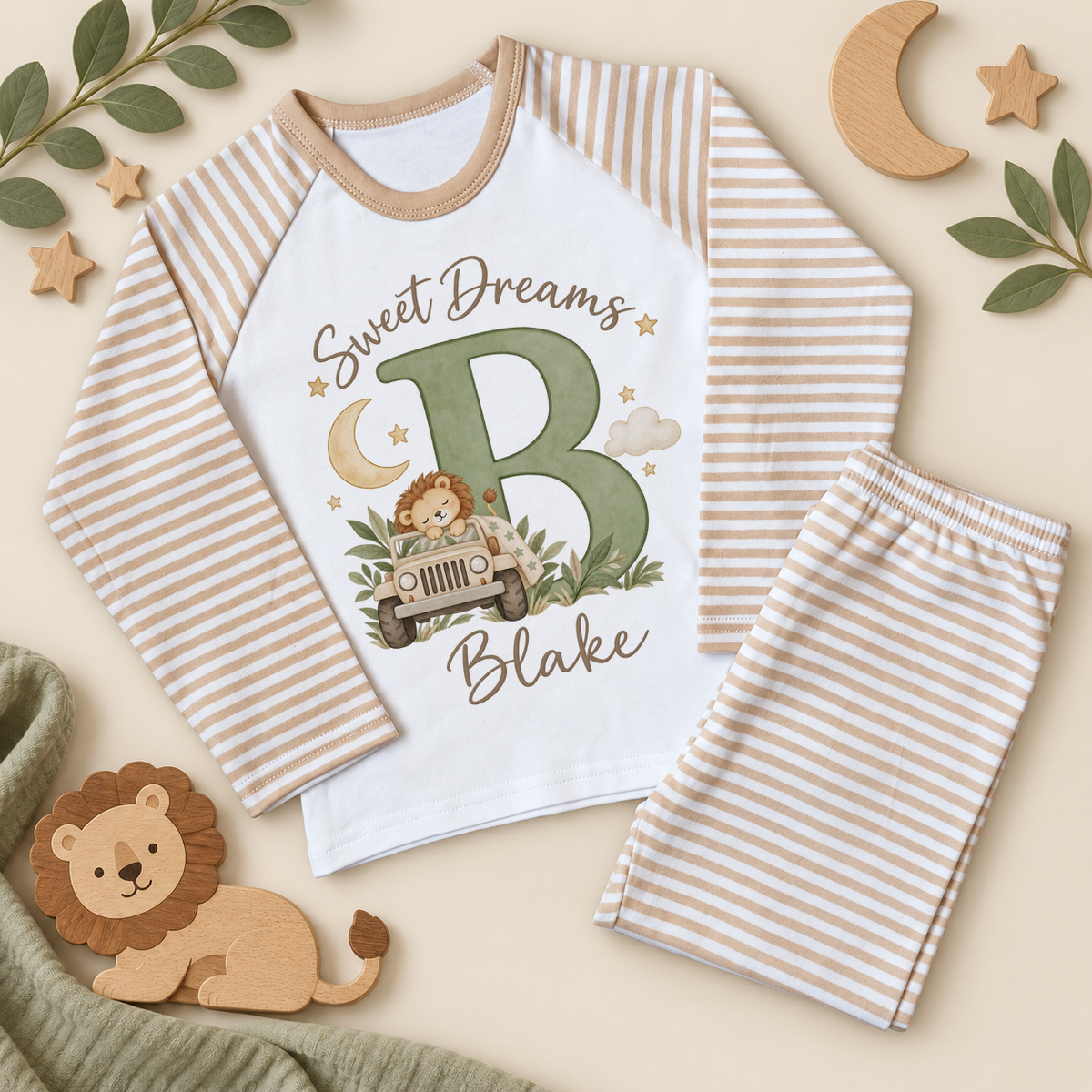 White raglan pyjama top printed with Sweet Dreams, a large sage green initial, a sleeping lion cub in a safari jeep and an example name in script, with beige striped sleeves and folded striped long trousers.