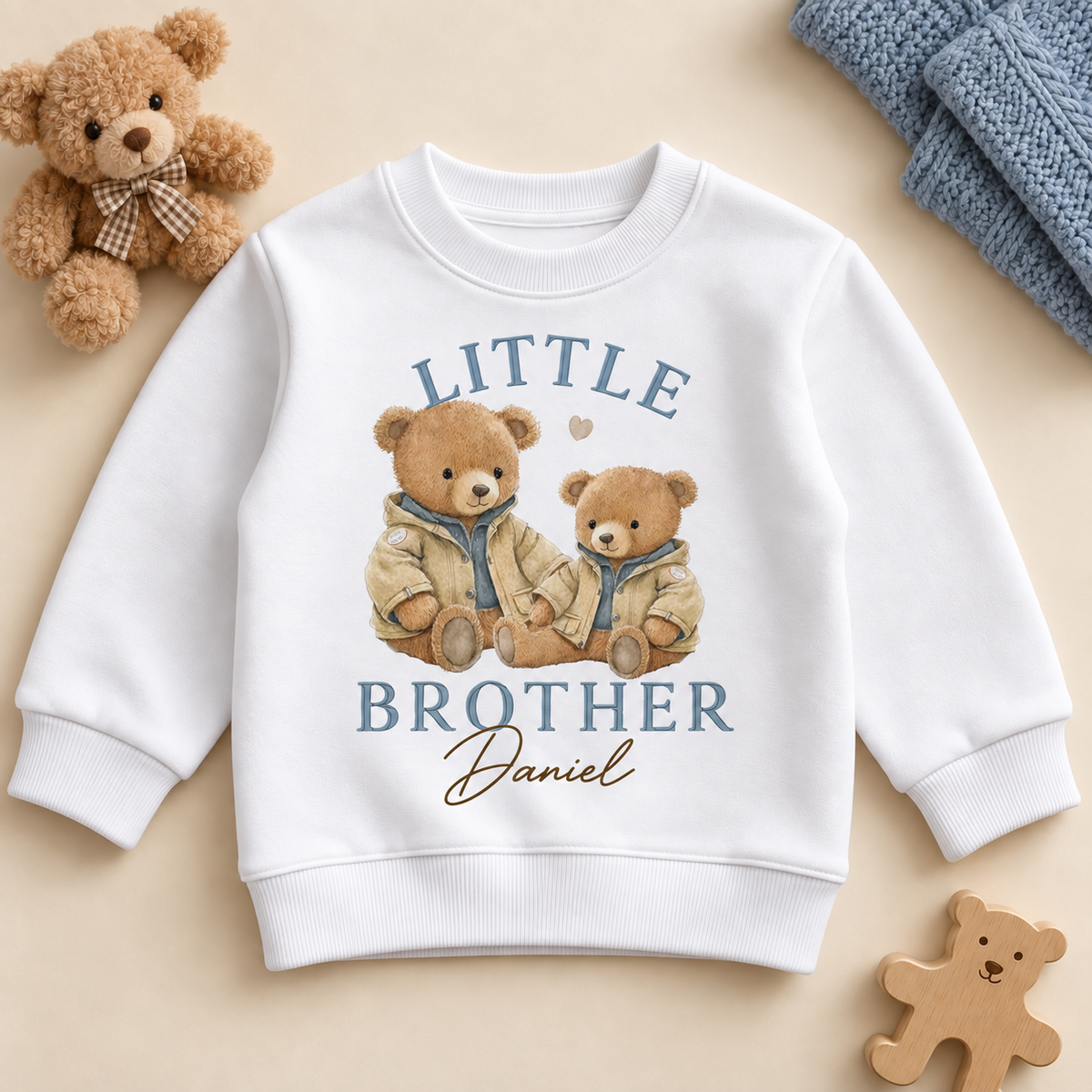 Personalised Little Brother white sweatshirt with two teddy bears in beige jackets and Daniel example name, on a cream flat lay.
